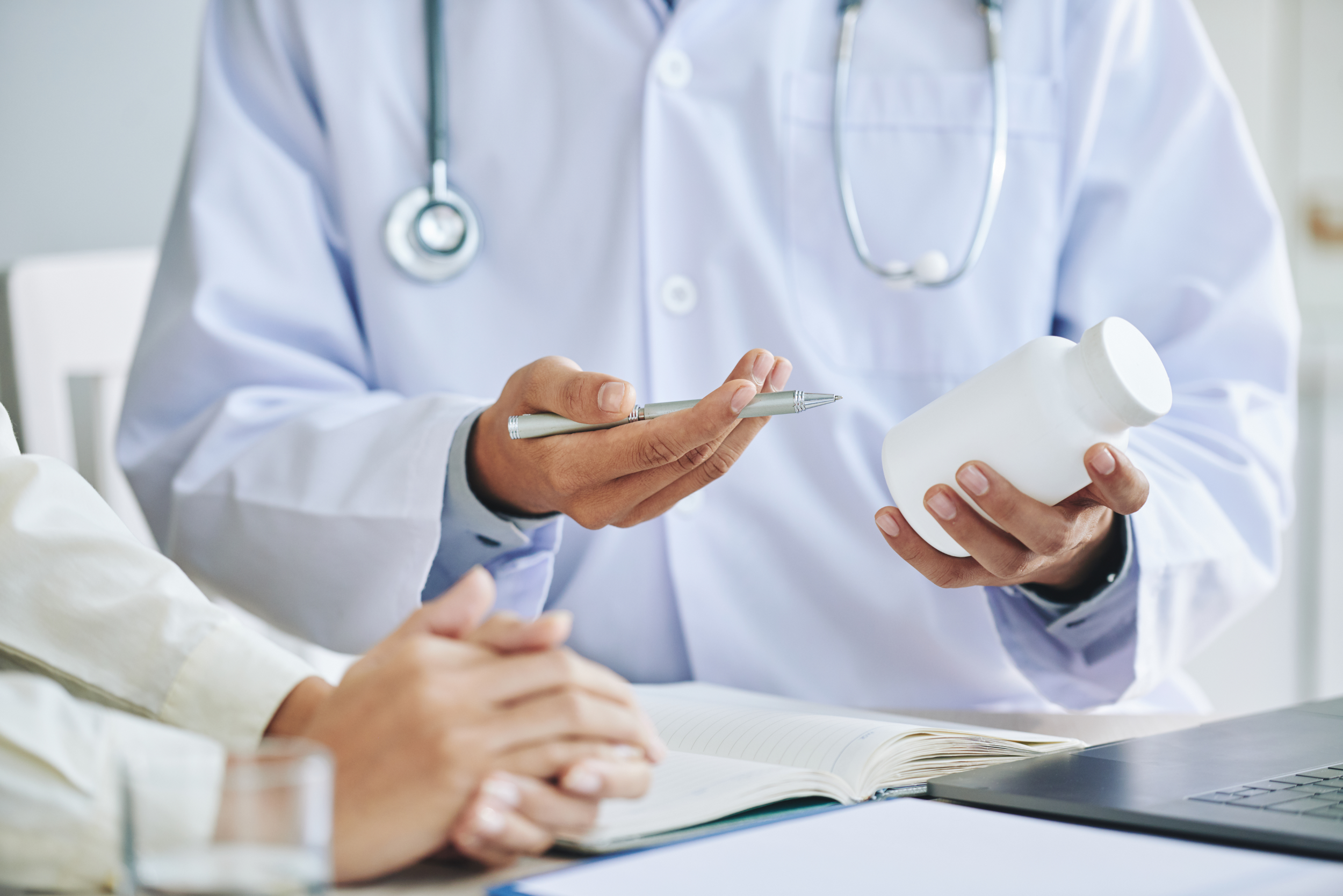 Male doctor holding a medicine bottle looking at its information while checking on his EMGuidance account on his laptop