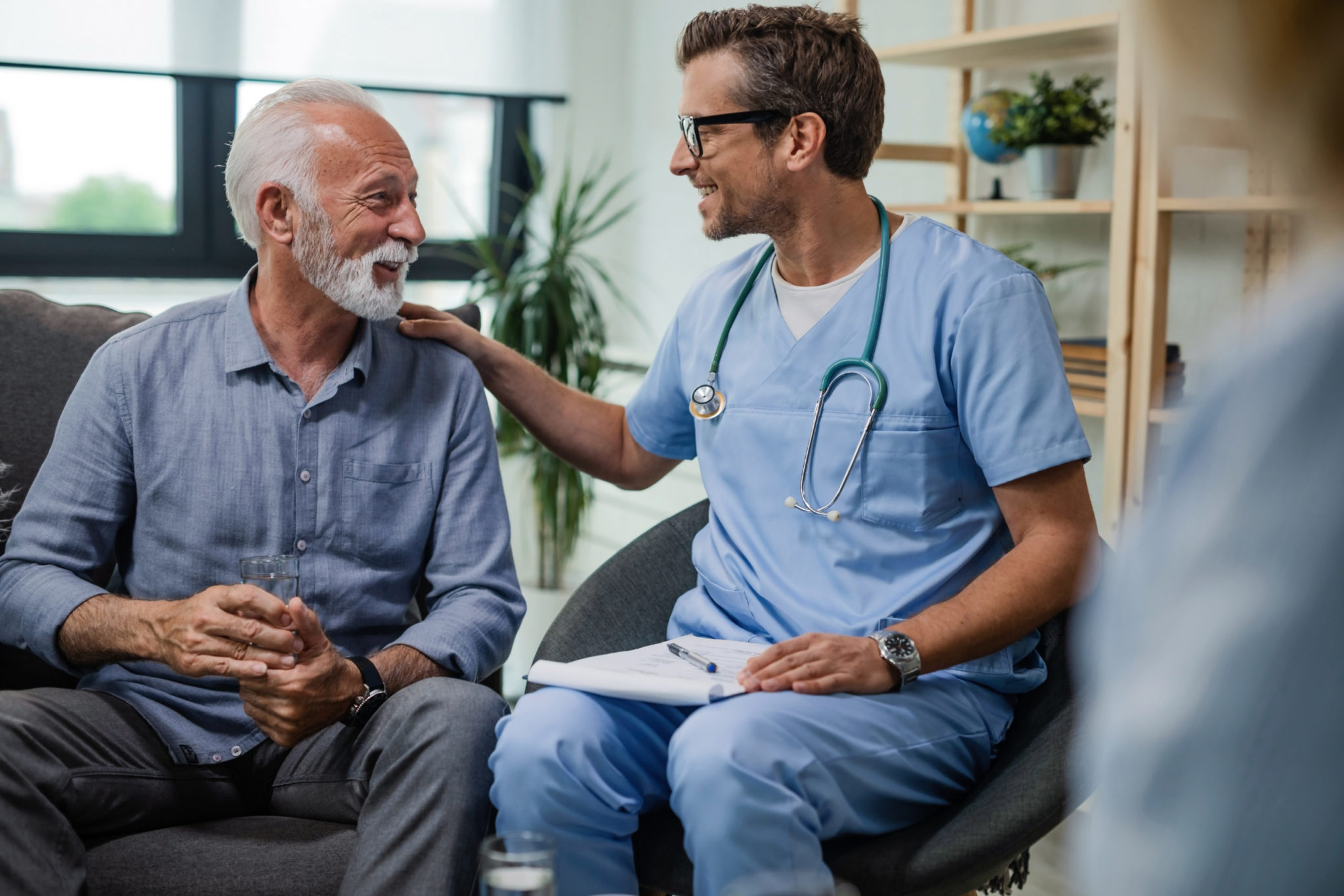 Happy doctor resting his hand on a happy elderly patient's shoulder